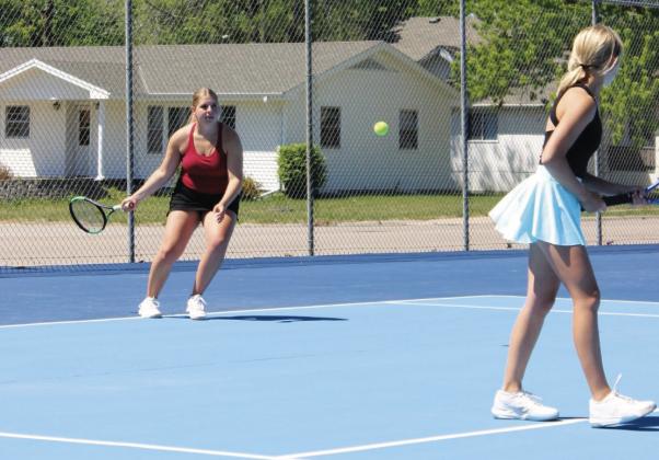 Peyton Hilbers plays a serve during a doubles match at York last week, while her teammate Briony Aden stays ready at the front of the court. (Leader photo by Megan Aden)