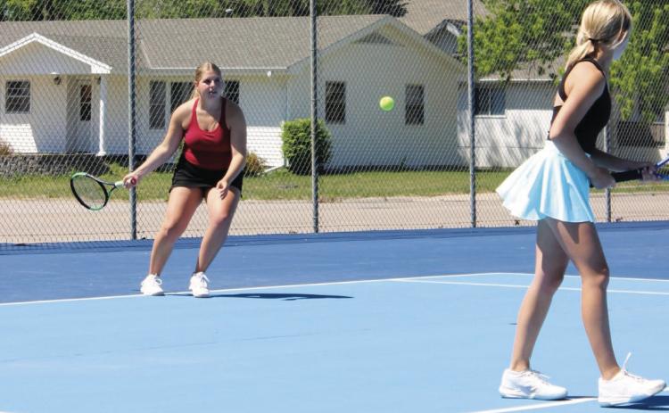 Peyton Hilbers plays a serve during a doubles match at York last week, while her teammate Briony Aden stays ready at the front of the court. (Leader photo by Megan Aden)